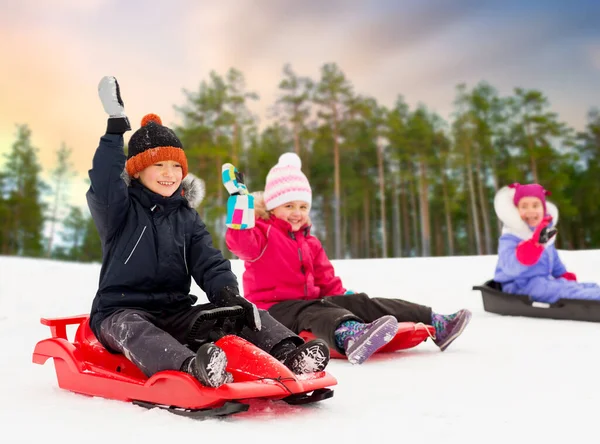 Glückliche kleine Kinder, die im Winter auf Schlitten rutschen — Stockfoto