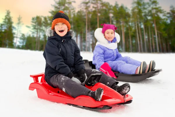 Glückliche kleine Kinder, die im Winter auf Schlitten rutschen — Stockfoto