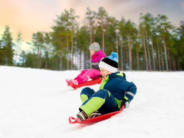 Crianças deslizando em trenós para baixo colina de neve no inverno — Fotografia de Stock