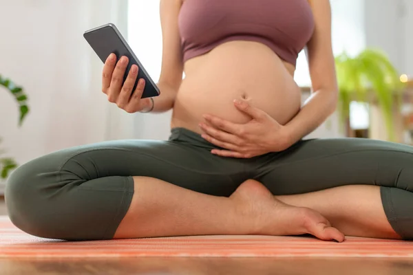 Close up of pregnant woman with phone doing yoga — Stock Photo, Image