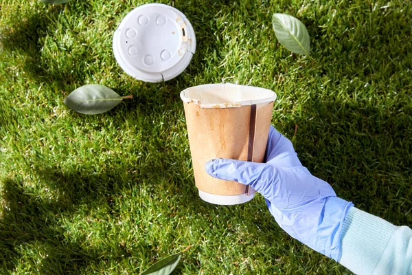 Primo piano di mano in guanto con tazza di caffè sull'erba — Foto Stock