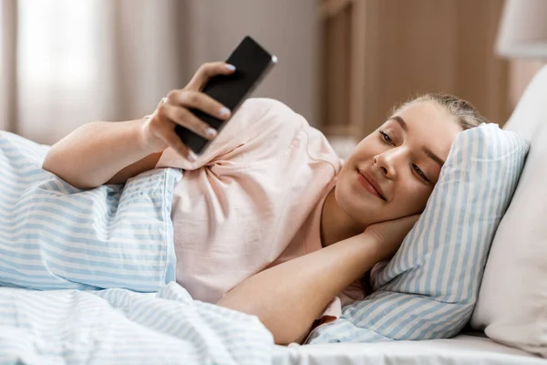 Chica feliz con teléfono inteligente en la cama en casa — Foto de Stock