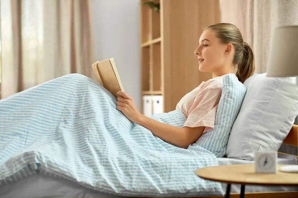 Sorrindo livro de leitura menina na cama em casa — Fotografia de Stock