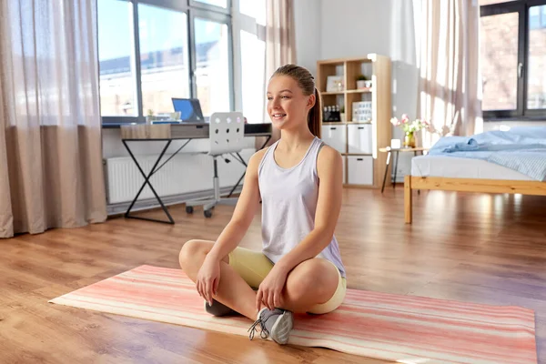 Улыбающаяся девочка-подросток сидит дома на коврике для йоги — стоковое фото
