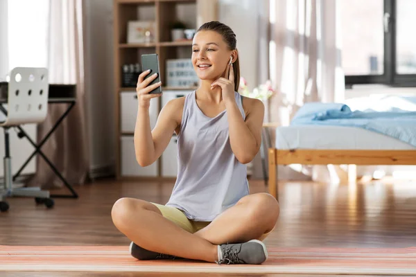 Chica con teléfono y auriculares haciendo ejercicio en casa — Foto de Stock