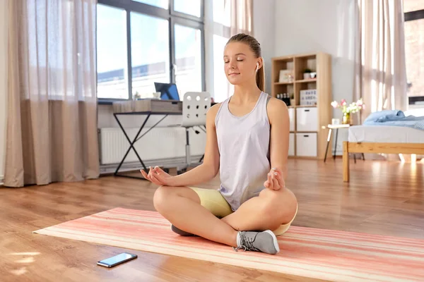 Meisje met telefoon en oortjes mediteren thuis — Stockfoto