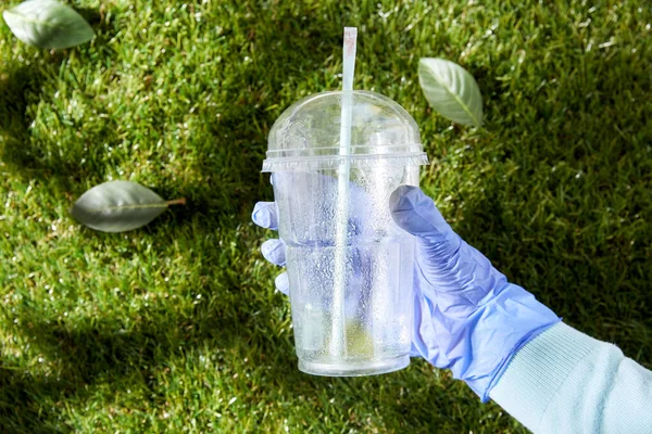 Main dans le gant enlever la tasse en plastique de l'herbe — Photo