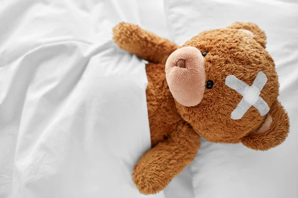 침대에 누운 머리 위에 의료 패치가 붙어 있는 곰 — 스톡 사진