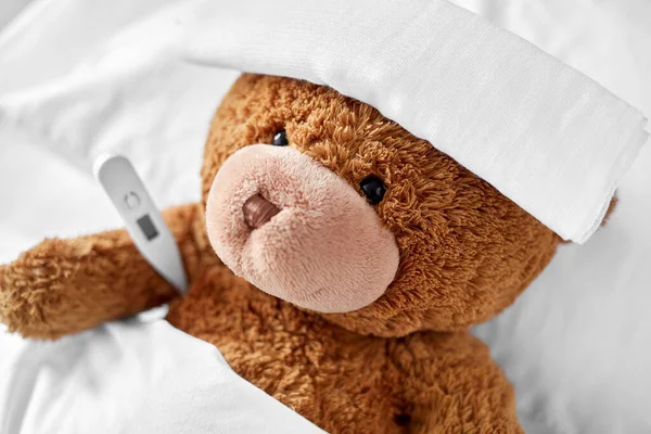 Ill teddy bear with bandage and thermometer in bed Stock Picture