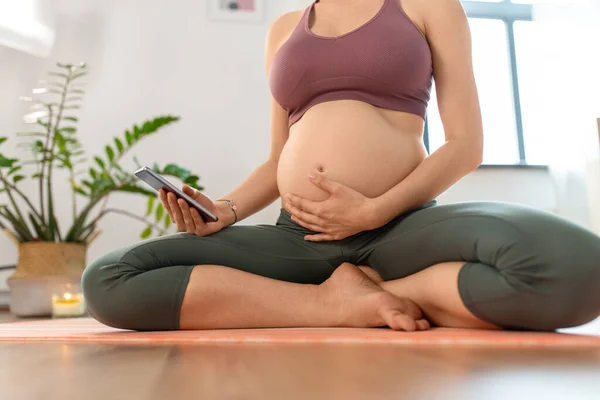 Close up of pregnant woman with phone doing yoga — Stock Photo, Image