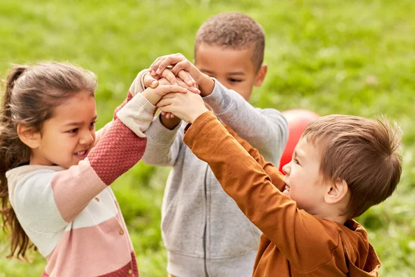 Crianças felizes brincando e empilhando as mãos no parque — Fotografia de Stock