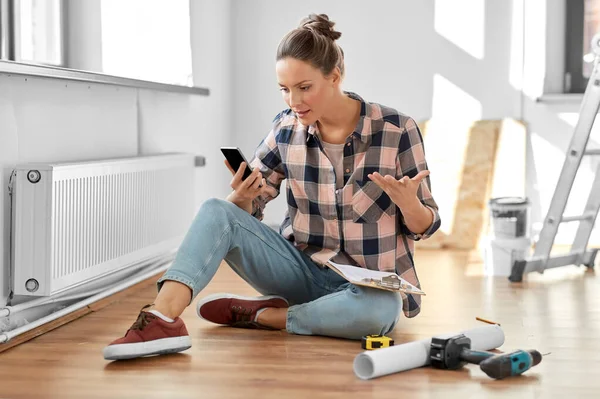 Angry woman with smartphone and clipboard at home — Stock Photo, Image