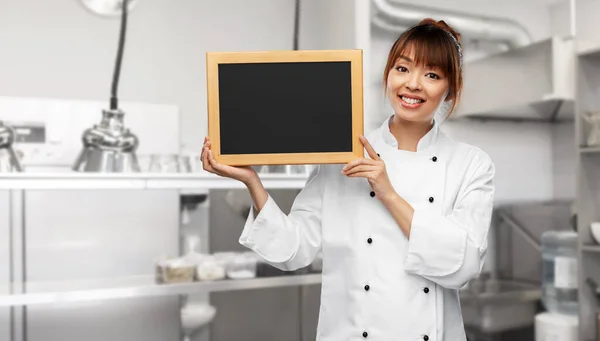 Köchin hält schwarze Tafel auf Küche — Stockfoto