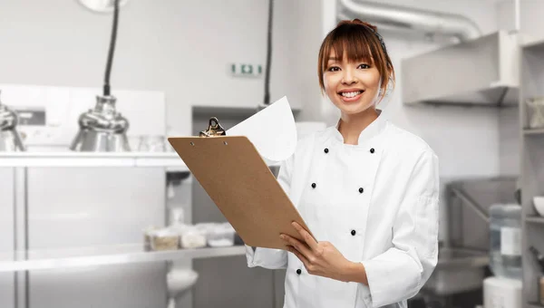 Glimlachende vrouwelijke chef met klembord op keuken — Stockfoto