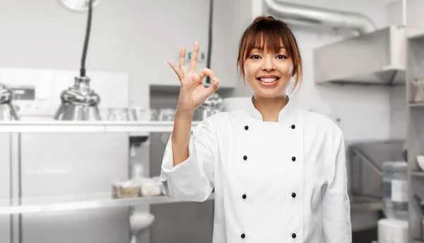 Happy female chef showing ok hand sign on kitchen Fotos De Bancos De Imagens