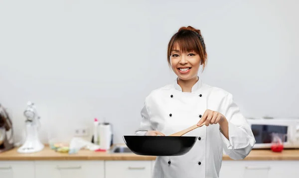 Glimlachende vrouwelijke chef-kok met koekenpan op keuken Stockfoto