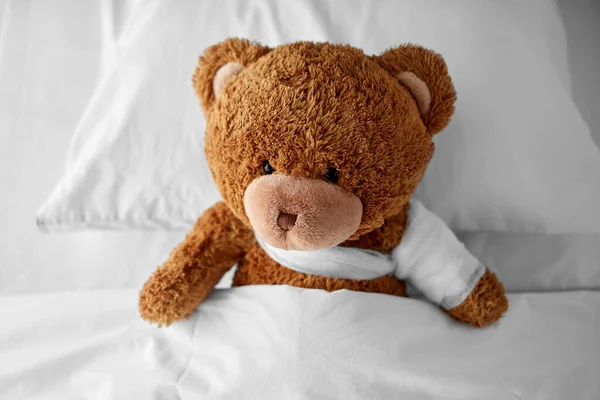 III medvídek hračka s obvázanou tlapkou v posteli — Stock fotografie