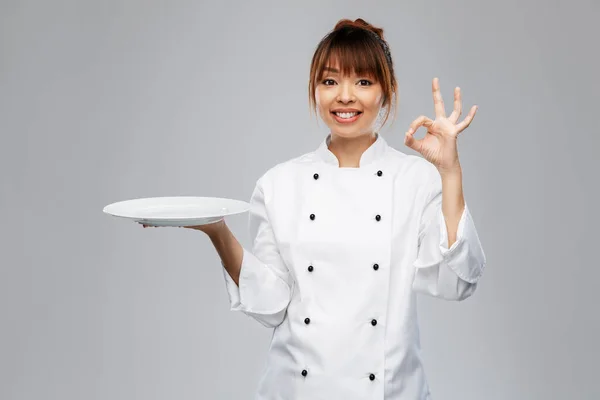 Female chef holding empty plate and showing ok — Foto Stock