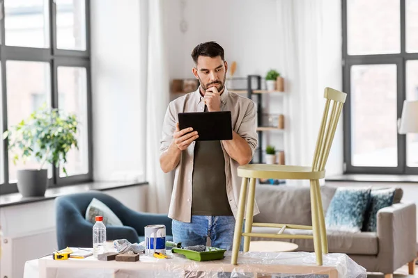 Hombre con tablet pc renovando silla vieja en casa —  Fotos de Stock