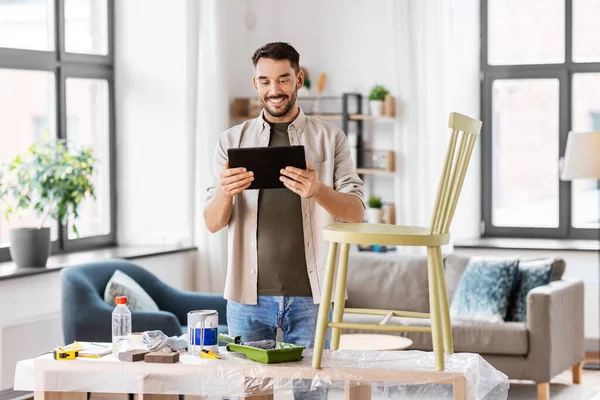 Hombre con tablet pc renovando silla vieja en casa —  Fotos de Stock