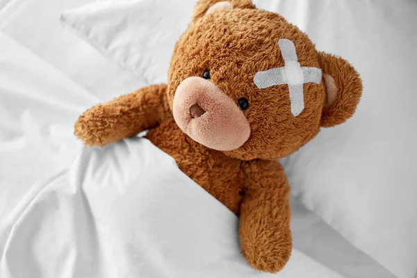 침대에 누운 머리 위에 의료 패치가 붙어 있는 곰 — 스톡 사진