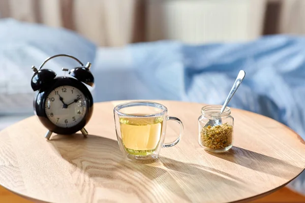 Despertador y taza de té de manzanilla en la mesa —  Fotos de Stock
