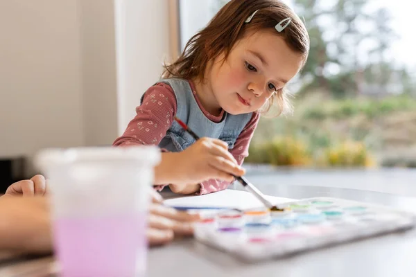 Baby girl with colors and brush drawing at home — Stockfoto