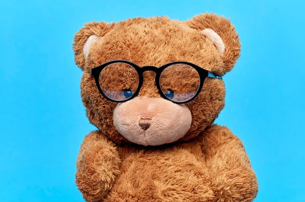 Игрушка медвежонка в очках на синем фоне — стоковое фото