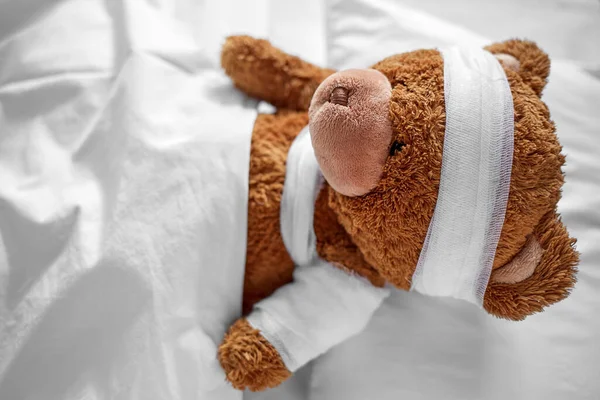 Sjuk nalle med bandage tass och huvud i sängen — Stockfoto