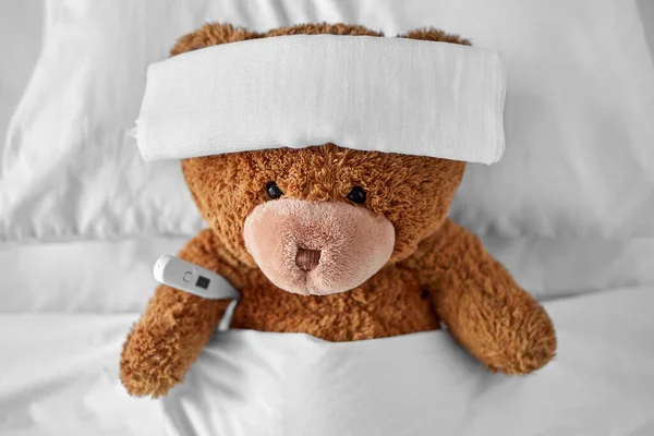 Ill teddy bear with bandage and thermometer in bed Royalty Free Stock Photos