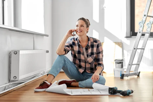 Woman with blueprint calling on smartphone at home — Stockfoto