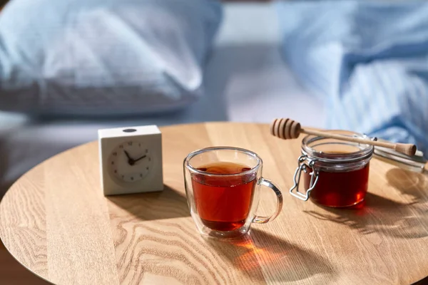 Cup of tea, honey and alarm clock on table — Fotografia de Stock