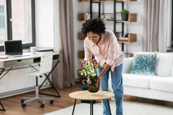 Mujer feliz colocando flores en la mesa en casa —  Fotos de Stock