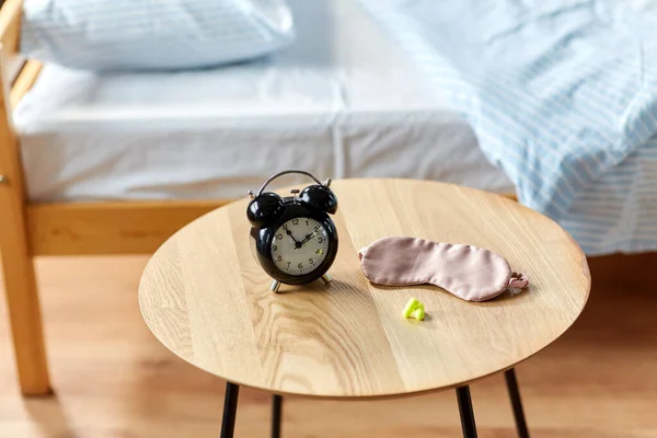 Despertador, tapones para los oídos y máscara para dormir en la mesa — Foto de Stock