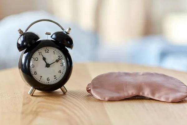 Alarm clock and eye sleeping mask on table at home — Stockfoto