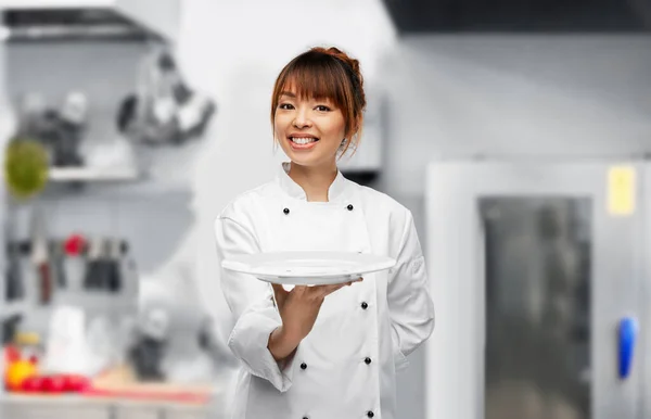 Feliz mujer chef sosteniendo plato vacío en la cocina —  Fotos de Stock