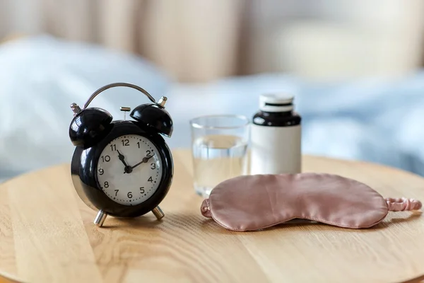alarm clock, mask and sleeping pills on table