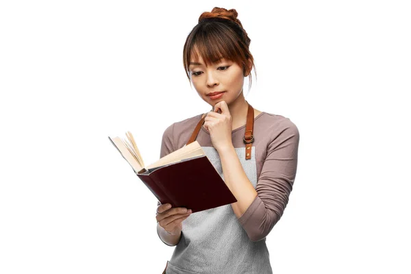 Thinking woman in apron reading cook book — Stock Fotó