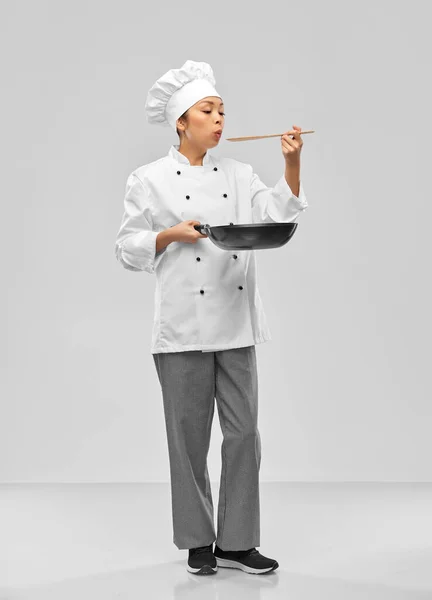 Female chef with frying pan blowing to spoon — стоковое фото