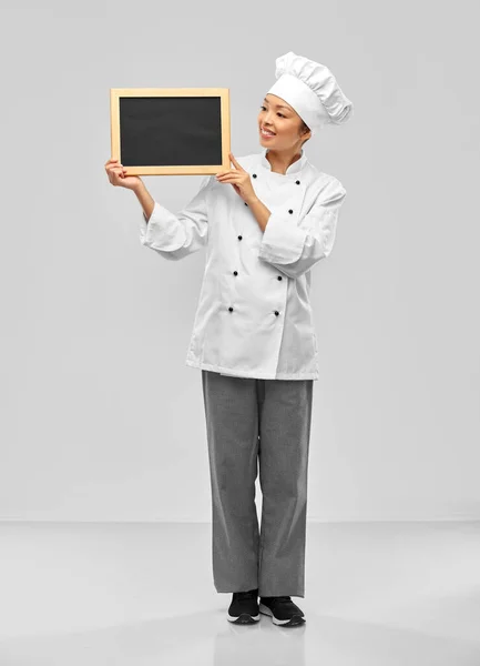 Glimlachende vrouwelijke chef met zwart schoolbord — Stockfoto