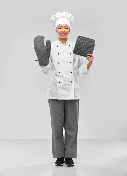 Smiling female chef in jacket with potholders — Stock Photo, Image