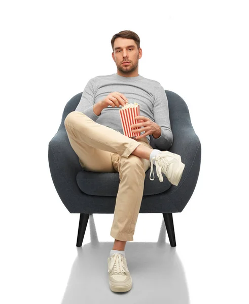 Bored man eating popcorn sitting in chair — Stock fotografie
