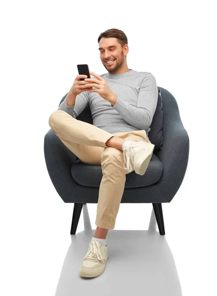 坐在椅子上，拿着智能手机快乐地微笑着的男人 — 图库照片