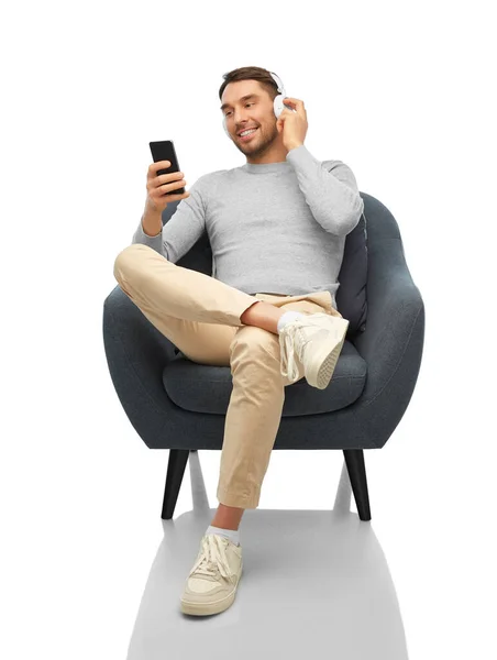 Мужчина с телефоном и наушниками сидит в кресле — стоковое фото