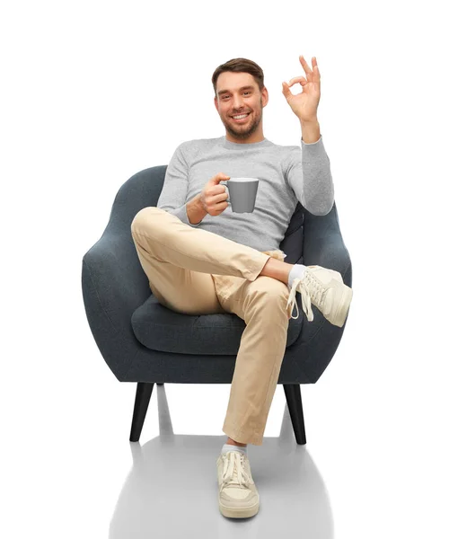 Man with mug showing ok gesture sitting in chair — Stock fotografie