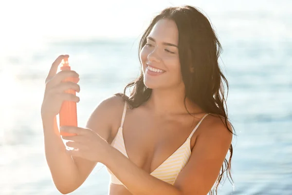 Uśmiechnięta kobieta w bikini z filtrem przeciwsłonecznym na plaży — Zdjęcie stockowe