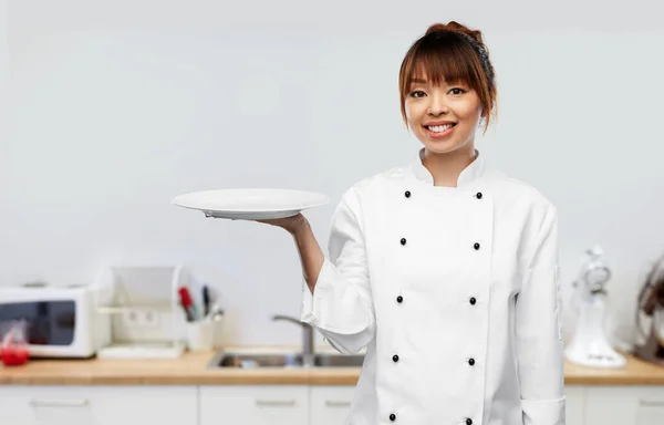 Happy female chef holding empty plate on kitchen Imagem De Stock