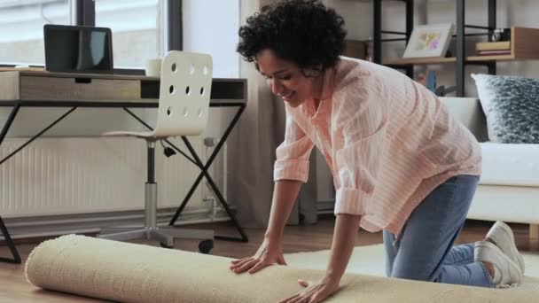 Smiling woman unfolding carpet at home — стоковое видео