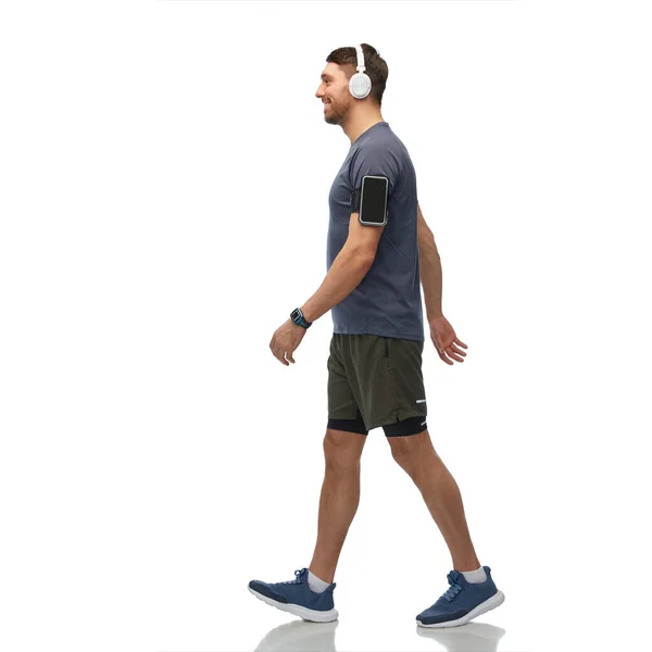 Usmívající se muž ve sluchátkách s chytrým telefonem chůze — Stock fotografie