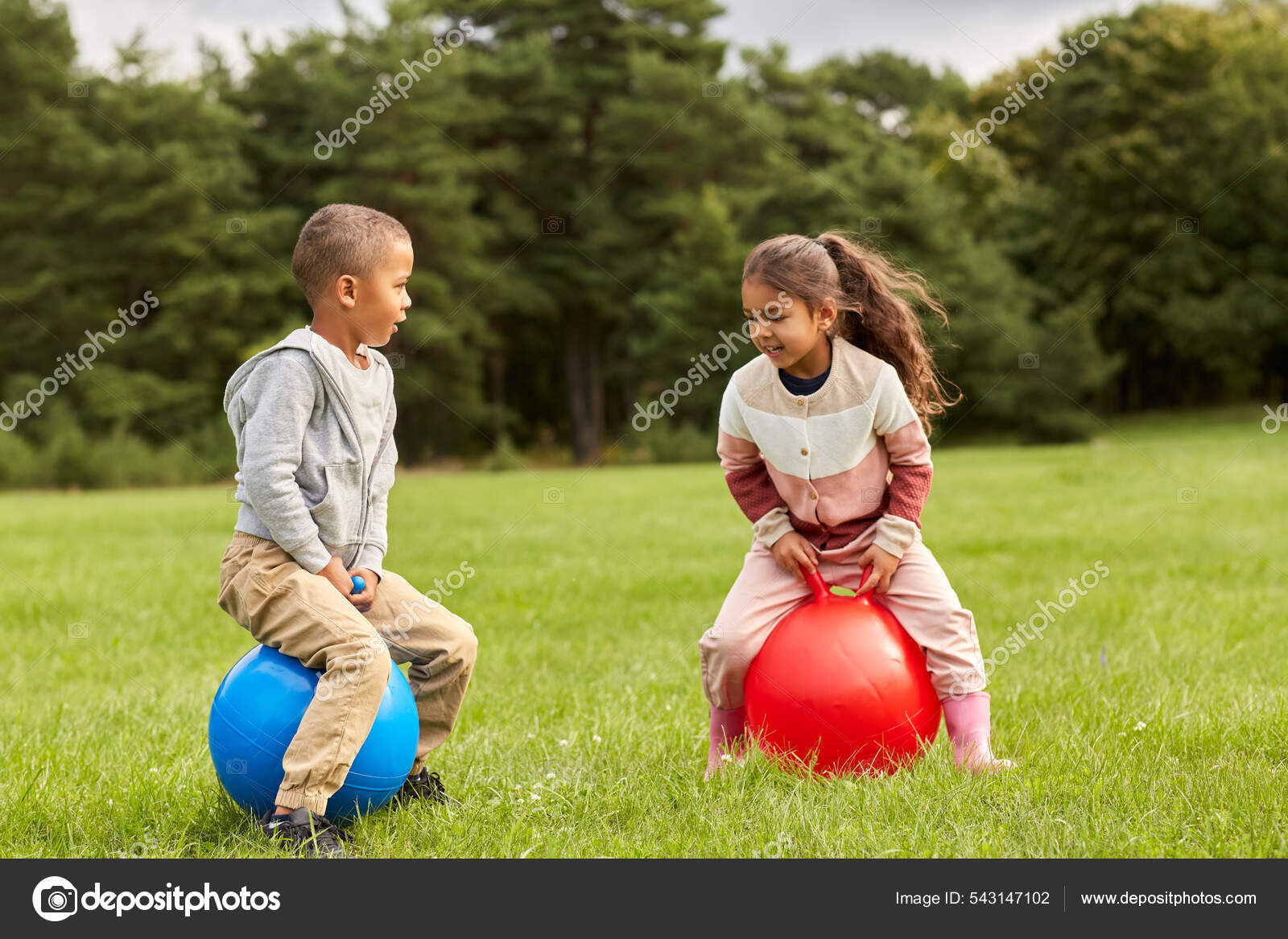 Happy children bouncing on hopper balls at park Stock Photo by ©Syda